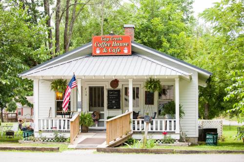 A charming café with a sign reading "Gap Creek Coffee House & Café," surrounded by greenery and featuring a welcoming porch.