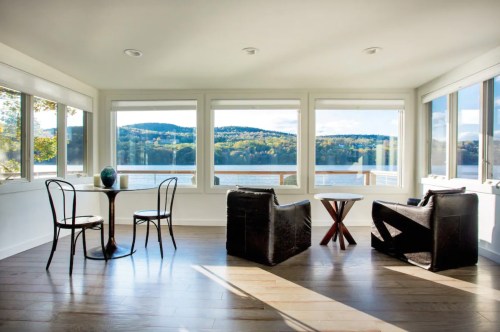Bright room with large windows overlooking a lake, featuring a round table and two black chairs.