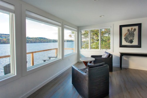 A cozy room with two chairs, a round table, and large windows overlooking a lake and hills.