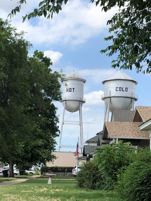 Two water towers labeled "HOT" and "COLD" stand against a blue sky, surrounded by trees and houses.