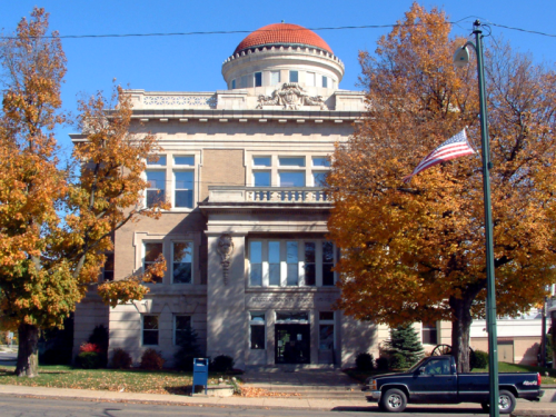 Historic building with a domed roof, surrounded by autumn trees and an American flag in front.