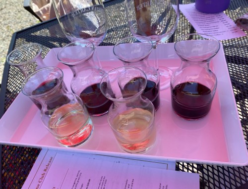 A tray with several small glass carafes of red and white wine, alongside empty wine glasses on a table.