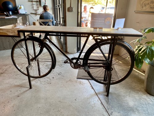 A unique table made from a bicycle frame, featuring a wooden top and set in a casual indoor space.