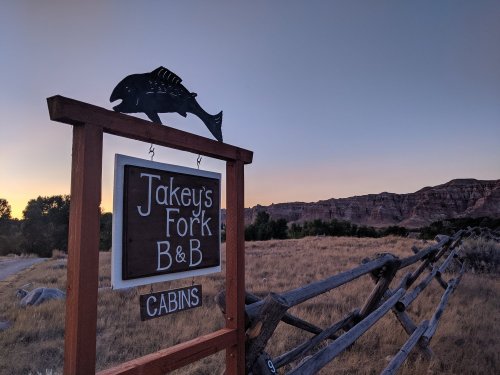 Sign for Jakey's Fork B&B with a fish silhouette, set against a sunset and rugged landscape.