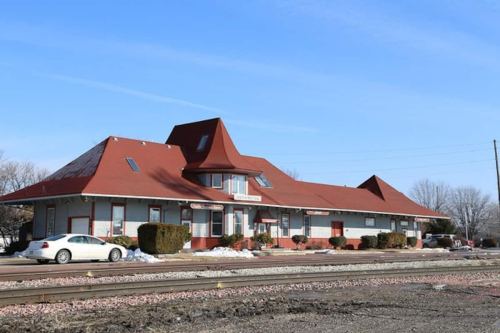 Historic train station with a distinctive red roof, surrounded by snow and a few parked cars.