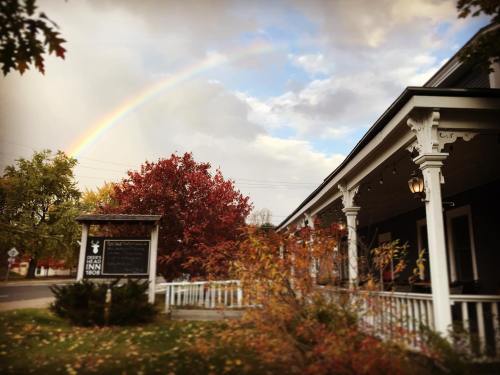 A charming inn with a porch, surrounded by colorful autumn foliage and a rainbow in the sky.