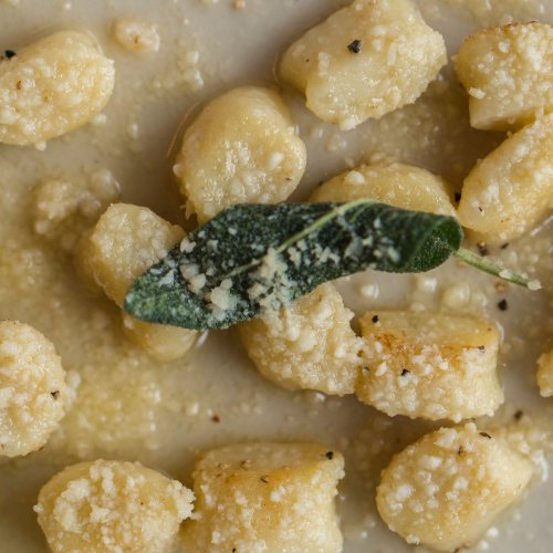 A close-up of gnocchi in a creamy sauce, topped with a sage leaf and sprinkled with grated cheese.