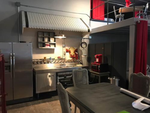 Modern kitchen with stainless steel appliances, a dining table, and a cozy, industrial design. Red accents add warmth.