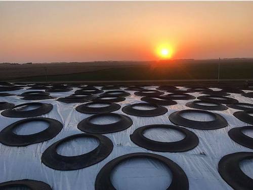 Sunset over a field, viewed from a rooftop with circular vents against a colorful sky.