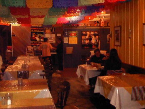 A cozy restaurant interior with colorful papel picado decorations, tables set for dining, and patrons enjoying their meals.