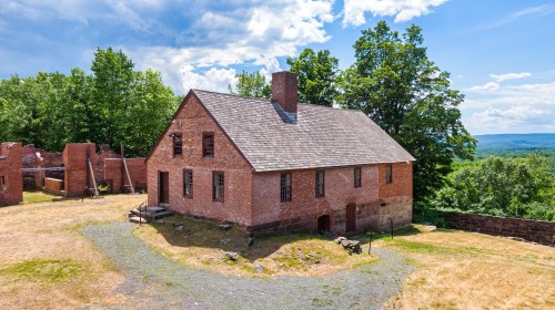 Historic brick building surrounded by greenery and ruins, set against a blue sky with scattered clouds.