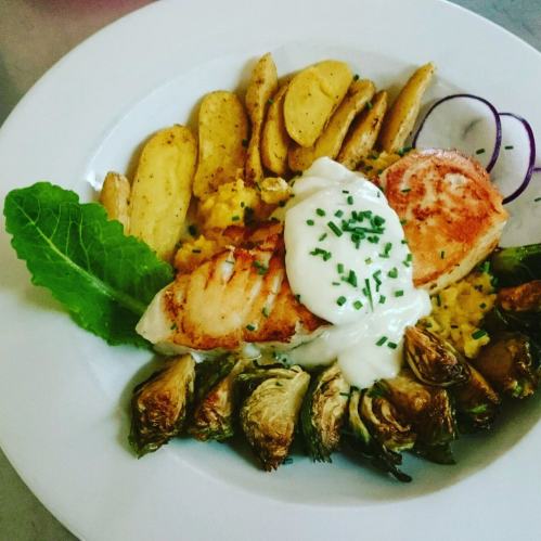 A plate of grilled salmon with creamy sauce, roasted potatoes, Brussels sprouts, and a side of lettuce.