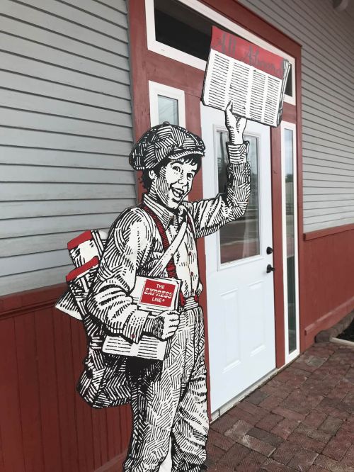A vintage-style illustration of a newspaper boy holding a newspaper, standing outside a building with a white door.