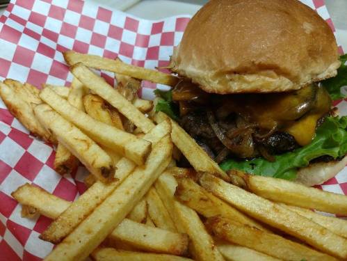 A juicy cheeseburger with lettuce and grilled onions, served with a side of golden French fries on a checkered paper.
