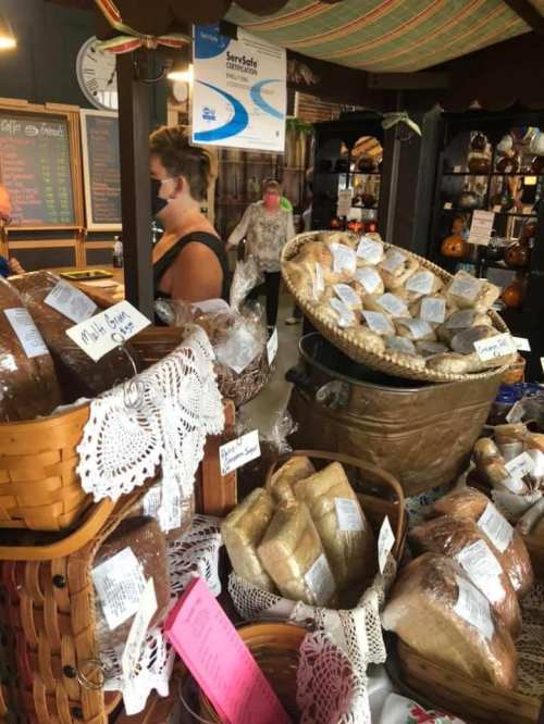 A market display featuring baskets of various baked goods, with shoppers in the background wearing masks.