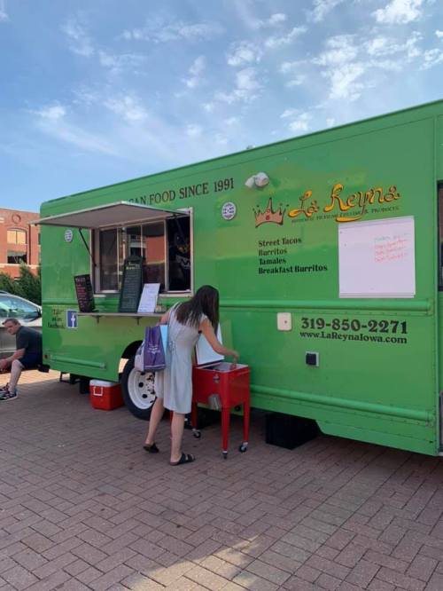 A green food truck with "La Reyna" signage, serving street tacos and burritos, with a customer at the ordering window.