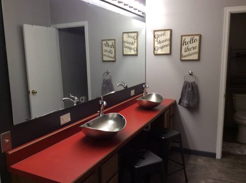 Modern bathroom with a red countertop, two stylish sinks, a large mirror, and decorative wall signs.