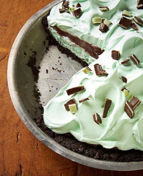 A mint chocolate pie with a creamy green topping and chocolate shavings, served in a metal pie dish.