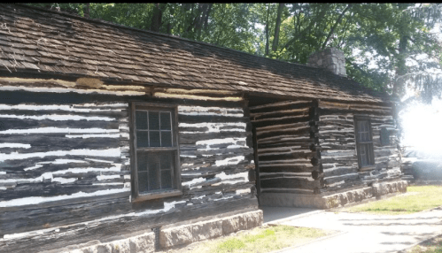 A rustic log cabin with a wooden exterior, featuring multiple windows and surrounded by trees.