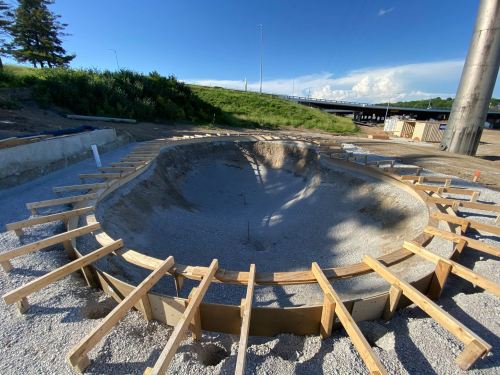 Construction site featuring a large, circular concrete structure surrounded by wooden framing and gravel.