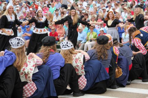 A group of dancers in traditional costumes perform in front of a large audience at an outdoor event.
