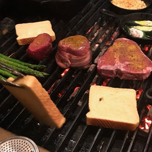 Grilling meat and bread on a barbecue, with asparagus and vegetables in cast iron pans.