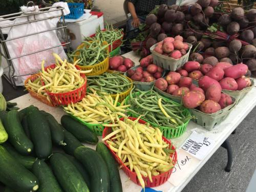 A vibrant display of fresh vegetables, including green beans, potatoes, cucumbers, and beets in colorful baskets.