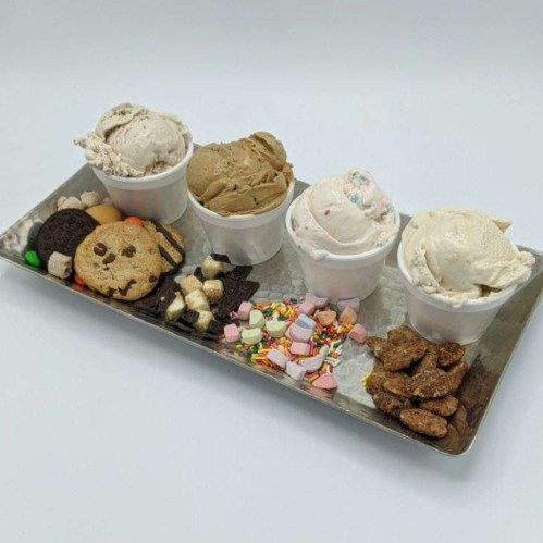 A tray with four cups of ice cream and various toppings, including cookies, sprinkles, and marshmallows.