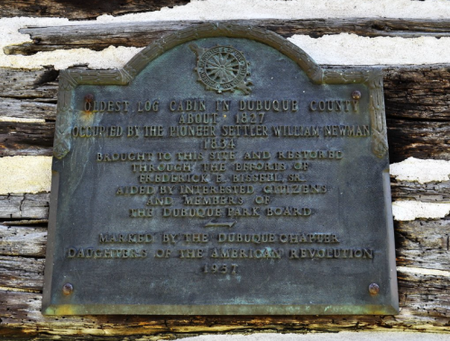 Plaque on a log cabin, detailing its history and restoration by local citizens and the Daughters of the American Revolution.