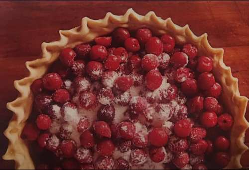 A pie crust filled with fresh red berries and sprinkled with sugar, set on a wooden surface.