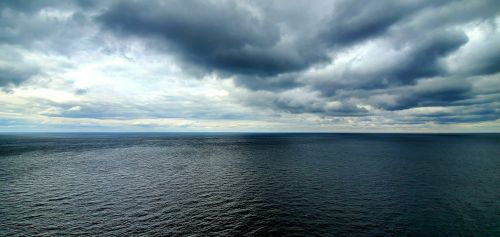 A vast ocean under a cloudy sky, with dark clouds reflecting on the calm water surface.