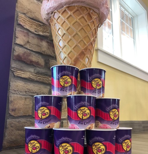 A large ice cream cone sculpture stands beside a stacked pyramid of ice cream tubs, all featuring colorful branding.