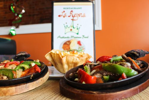 Sizzling fajitas with colorful peppers on a wooden platter, alongside a menu for La Reyna restaurant.