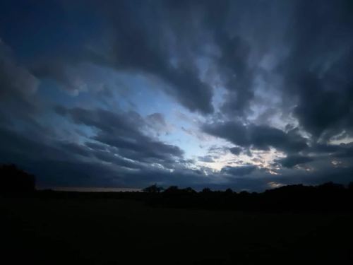 A dramatic sky filled with dark clouds and hints of blue, transitioning to twilight over a silhouetted landscape.
