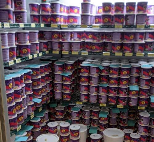 A large display of colorful ice cream tubs stacked on shelves in a freezer.