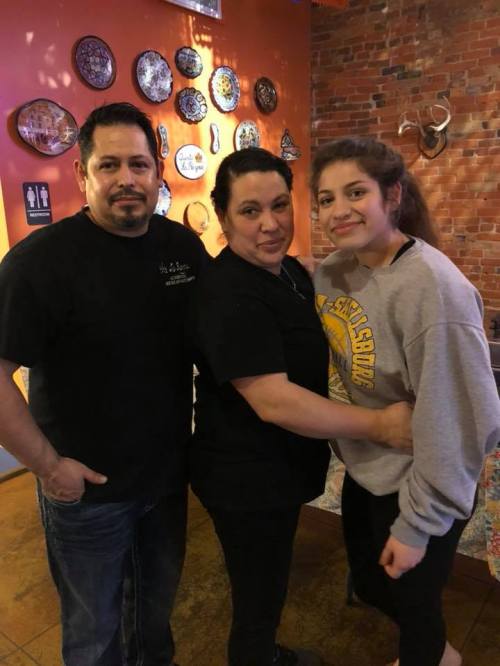 A family poses together in a restaurant, smiling, with decorative plates on the wall behind them.