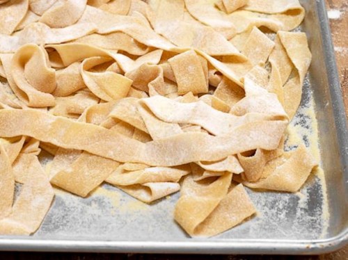 Freshly made pasta strips dusted with flour on a baking sheet.