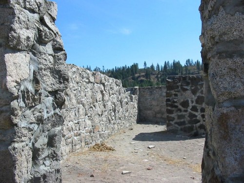 Stone ruins with weathered walls, surrounded by trees and a clear blue sky.