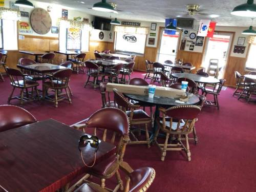 A cozy restaurant interior with wooden tables, chairs, and red carpet, featuring decor and empty seating.