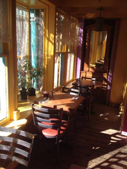 Brightly lit restaurant interior with colorful windows, wooden tables, and chairs, creating a warm, inviting atmosphere.