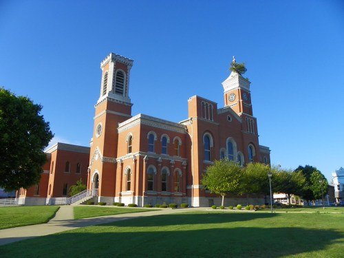 Historic brick church with clock towers, surrounded by green lawns and clear blue sky.