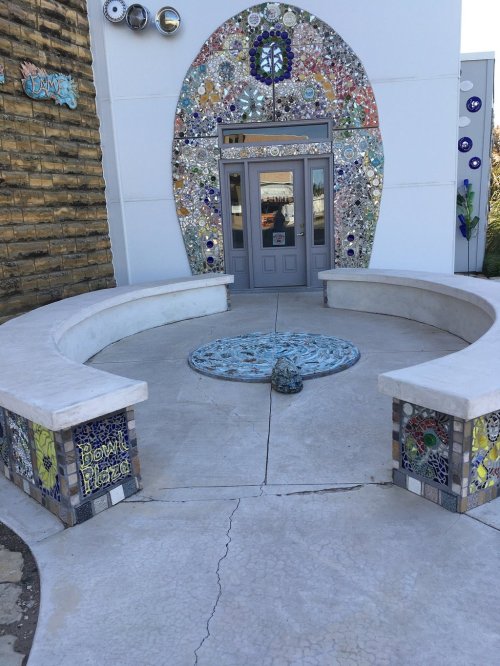 A colorful mosaic entrance with a circular design and curved benches in front of a door.