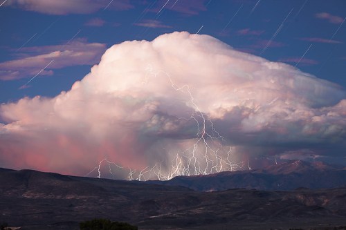 A dramatic cloud formation illuminated by lightning, set against a twilight sky and distant mountains.
