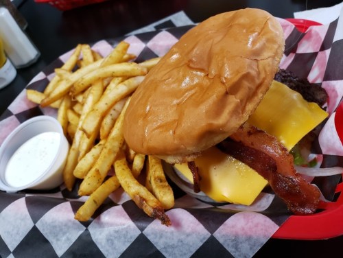 A juicy cheeseburger with bacon, lettuce, and tomato, served with crispy fries and a side of ranch dressing.