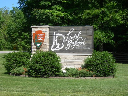 Sign for Lincoln Boyhood National Memorial, featuring park logo and name, surrounded by greenery.