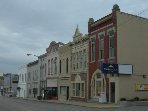 Historic buildings line a quiet street, featuring a mix of architectural styles and a bank sign.