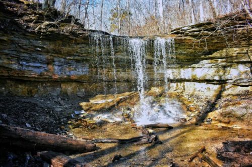 A serene waterfall cascading over rocky cliffs, surrounded by trees and a peaceful forest setting.