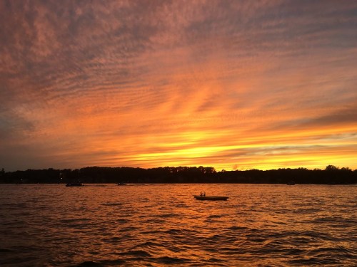 A vibrant sunset over a calm lake, with colorful clouds reflecting on the water and silhouettes of trees in the background.