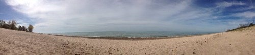 A panoramic view of a sandy beach with calm waters and a cloudy sky in the background.