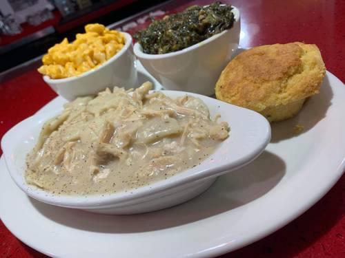 A plate featuring chicken and dumplings, macaroni and cheese, collard greens, and a cornbread muffin.